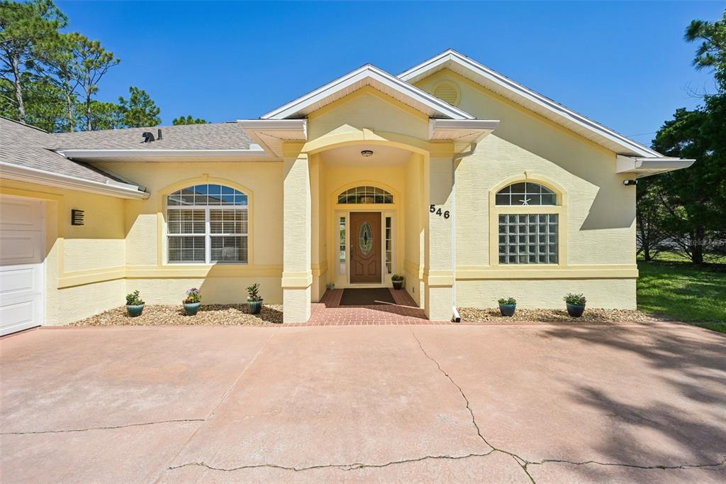 A yellow single-story house with a covered entryway, arched windows, and a concrete driveway — 546 SEVILLA DRIVE, ST AUGUSTINE, FL