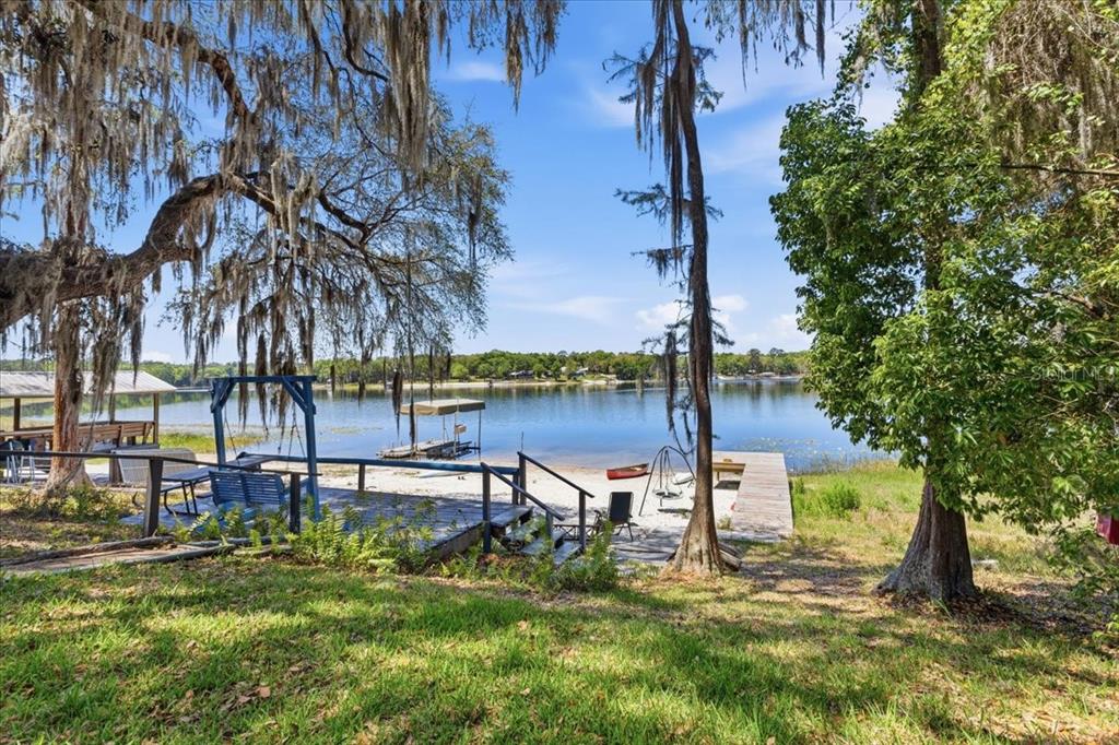 A wooden deck and dock overlook a calm lake framed by moss-draped trees — 8386 AUSTIN ROAD, MELROSE, FL