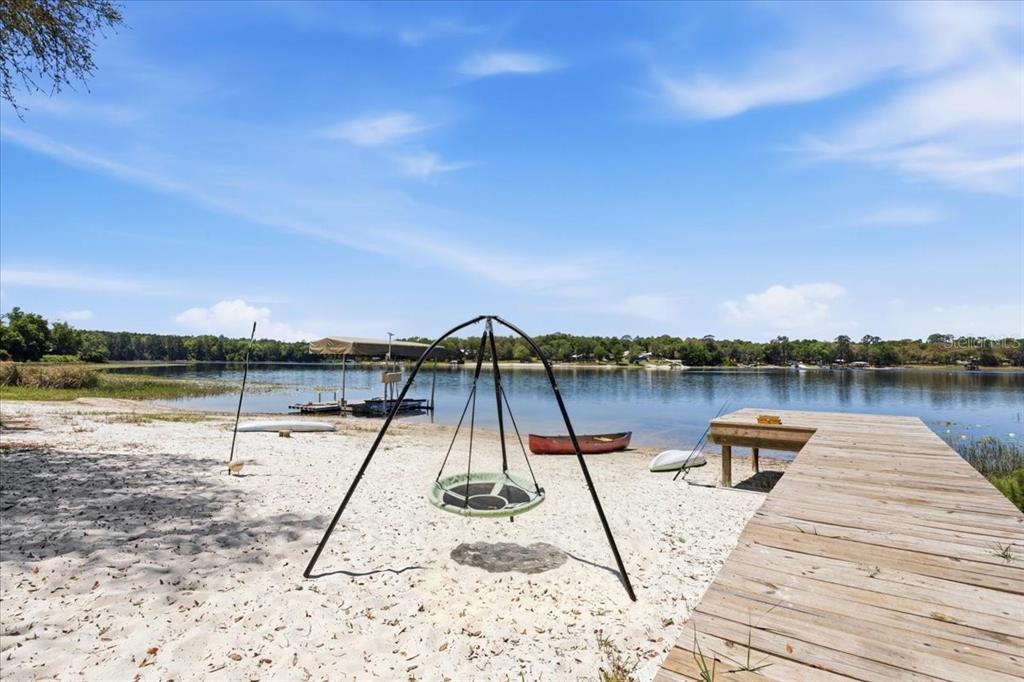 A sandy beach area features a swing set, a wooden dock, and a lake view — 8386 AUSTIN ROAD, MELROSE, FL