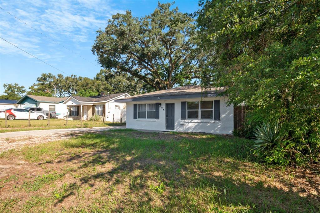 A white single-story house with dark shutters sits on a grassy lot under large trees — 341 AVENUE L NE, WINTER HAVEN, FL