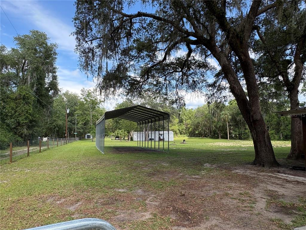 A large metal carport stands in a grassy yard shaded by mature oak trees — 15190 NE 144TH STREET, FORT MC COY, FL
