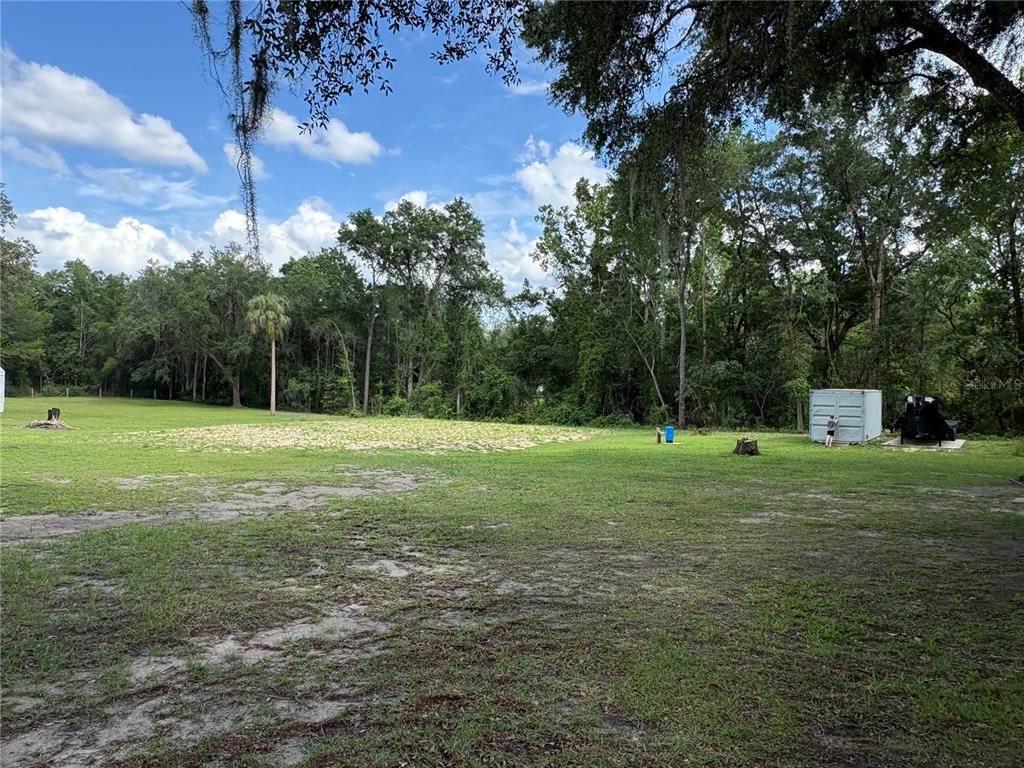 A large, grassy backyard features a sandy patch, scattered trees, and a storage container — 15190 NE 144TH STREET, FORT MC COY, FL