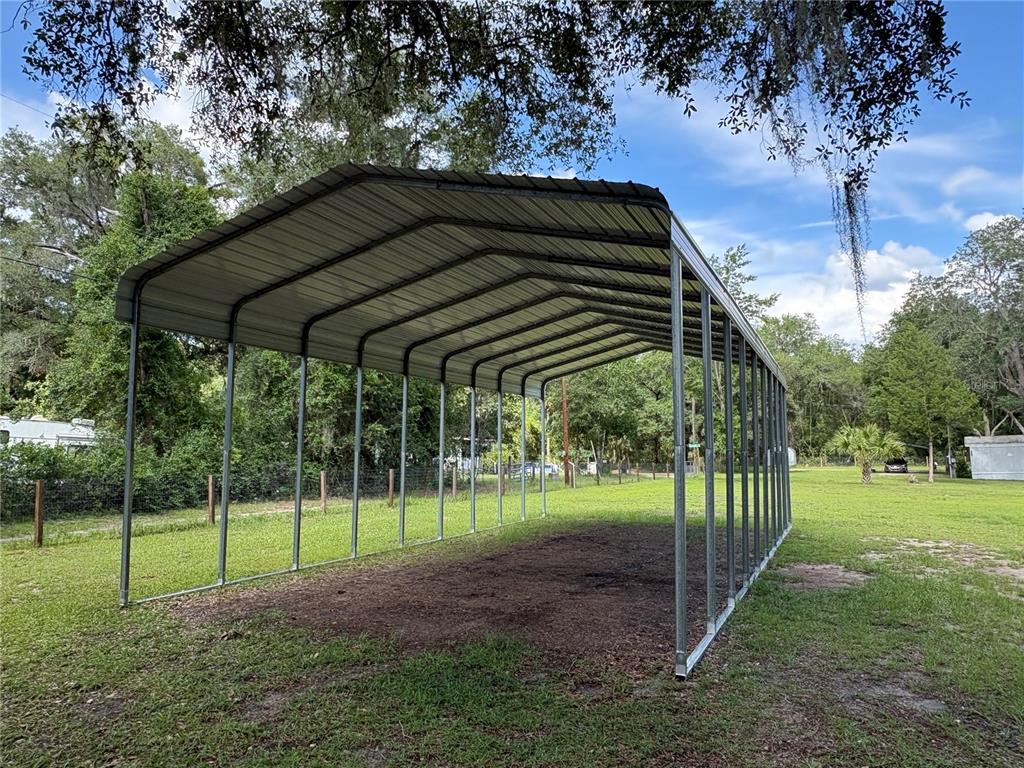 A metal carport structure stands in a grassy yard surrounded by trees — 15190 NE 144TH STREET, FORT MC COY, FL