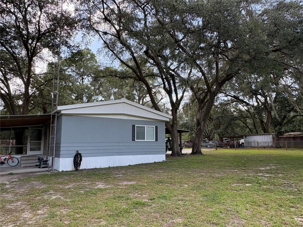 A gray mobile home with a white skirt sits on a grassy lot under trees — 15190 NE 144TH STREET, FORT MC COY, FL