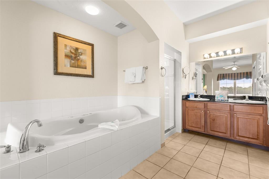 A bathroom features a white soaking tub, a double vanity with wood cabinets, and tile flooring — 8100 POINCIANA BOULEVARD UNIT 2505, ORLANDO, FL
