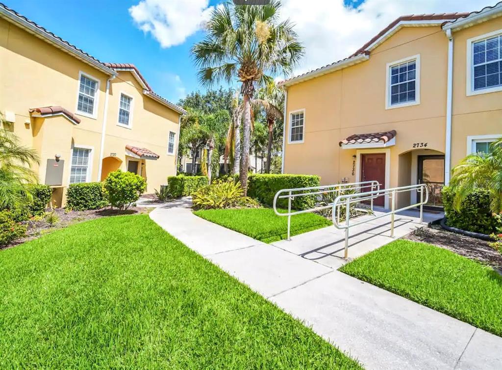 A sidewalk leads to the entrances of two yellow stucco townhomes with metal railings — 2736 OAKWATER DRIVE, KISSIMMEE, FL