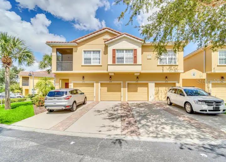 A two-story tan townhouse features a two-car garage and two parked SUVs in the driveway — 2736 OAKWATER DRIVE, KISSIMMEE, FL