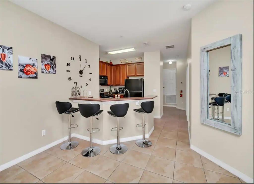A kitchen with a breakfast bar, four stools, and a wall-mounted clock in an apartment — 2736 OAKWATER DRIVE, KISSIMMEE, FL