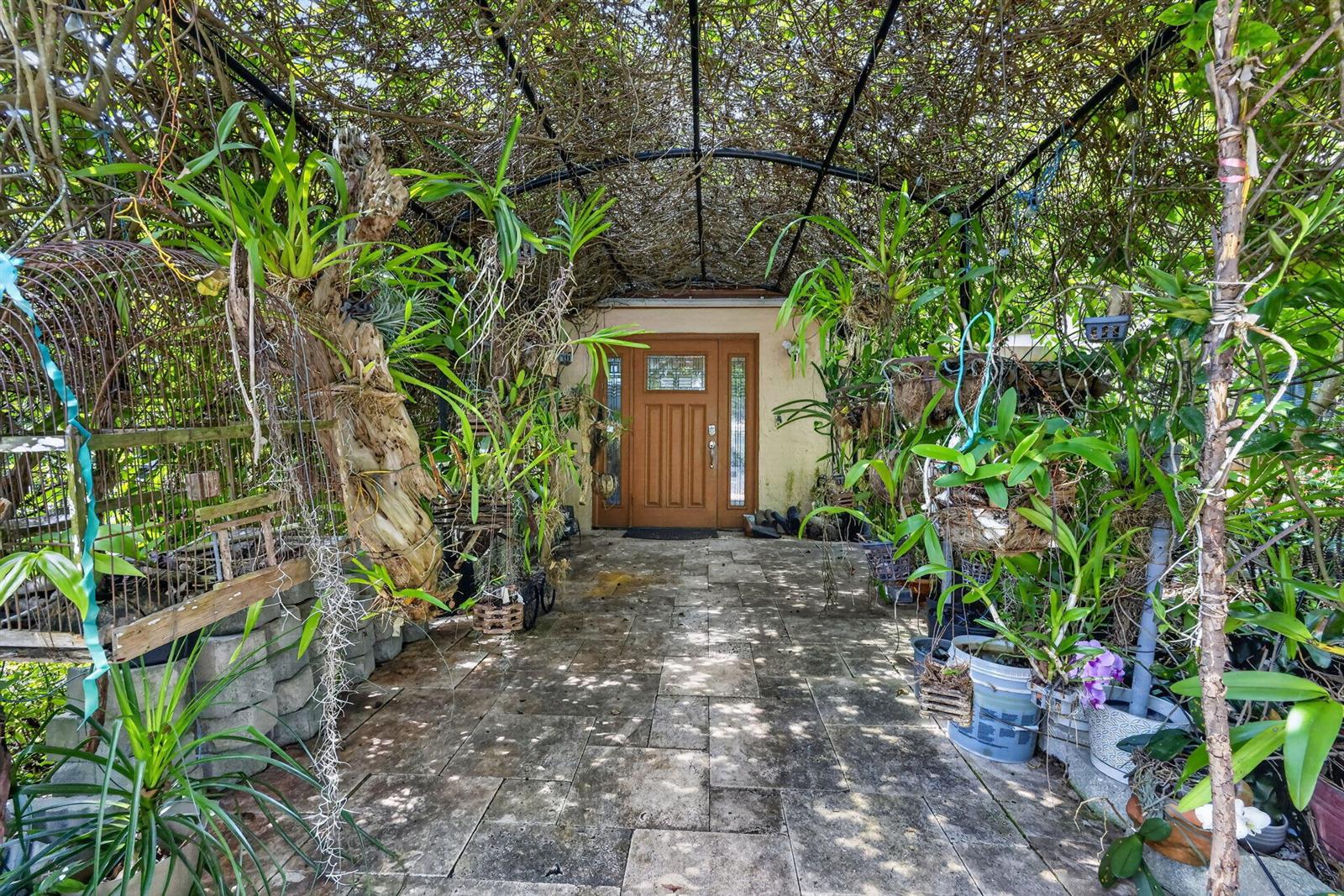 A stone-paved entryway features a wooden door framed by an overhead trellis covered in plants — 6022 Western Way, Lake Worth FL 33463, LAKE WORTH, FL