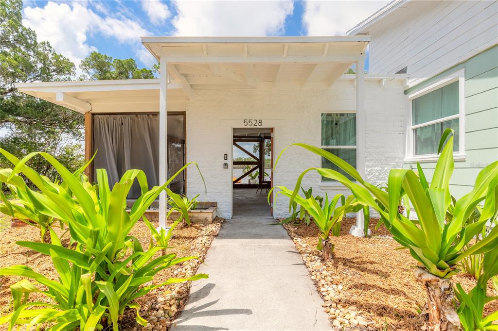 A concrete walkway leads to the covered entrance of a white house with landscaping — 5528 W BAYSHORE DRIVE, PORT ORANGE, FL