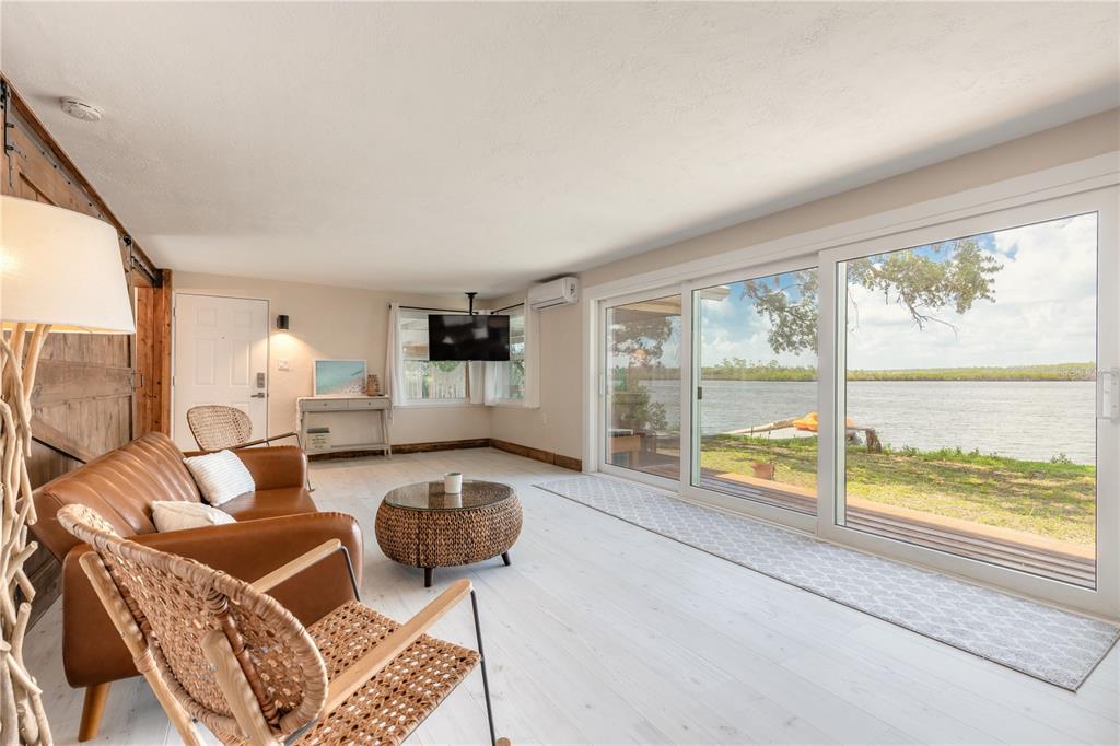 A living room with a leather sofa, wicker chairs, and large sliding doors overlooking water — 5528 W BAYSHORE DRIVE, PORT ORANGE, FL