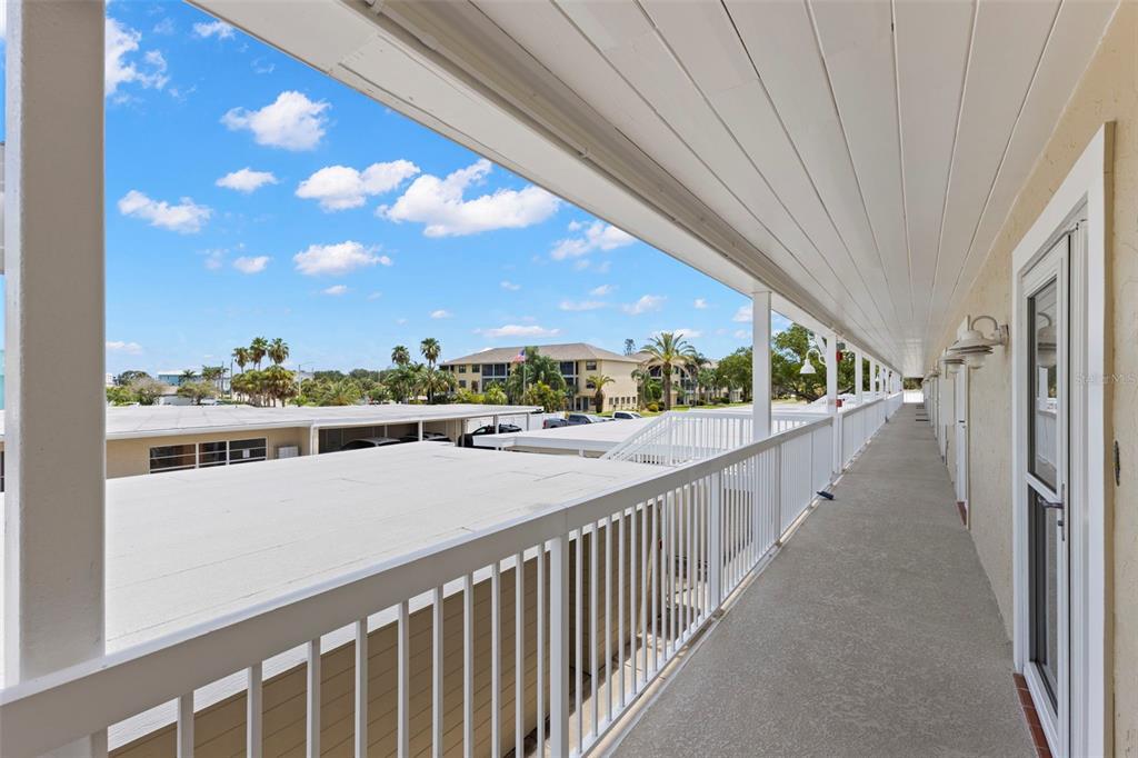An outdoor covered walkway with a white railing overlooks a parking lot and apartment buildings — 433 S PAULA DRIVE UNIT 28, DUNEDIN, FL