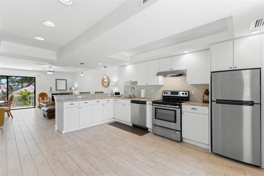 A bright kitchen with white cabinets, stainless steel appliances, and light wood-look tile flooring — 433 S PAULA DRIVE UNIT 28, DUNEDIN, FL