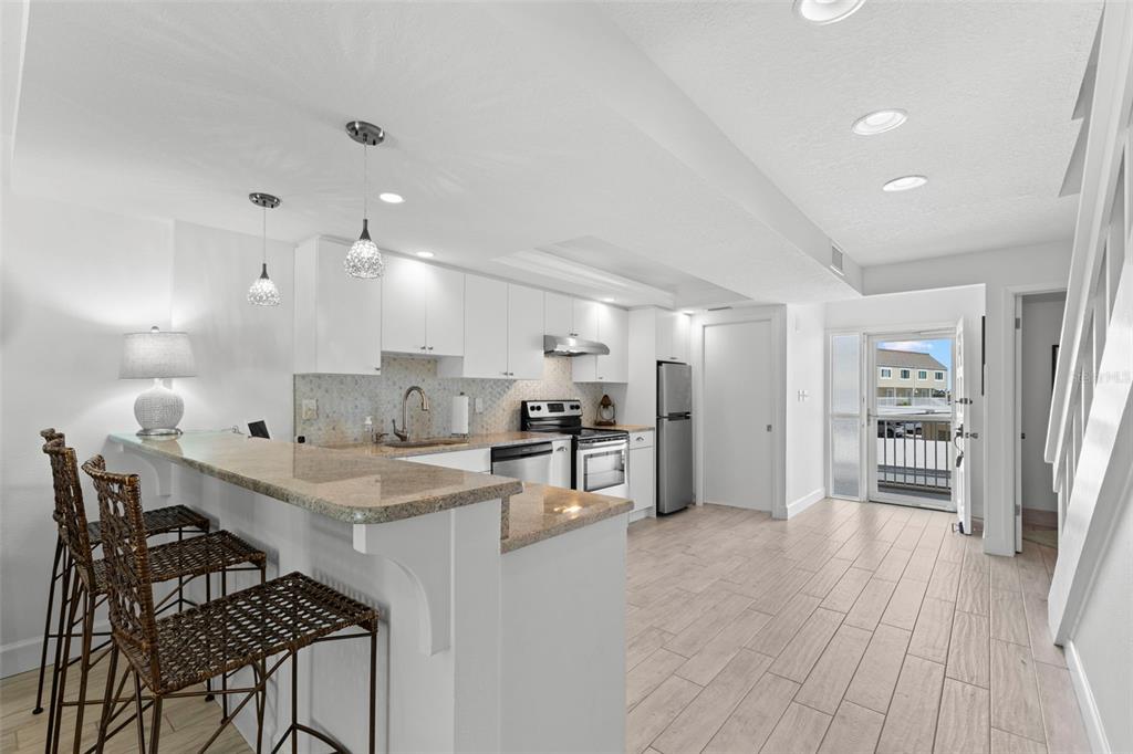 A bright kitchen features white cabinets, granite countertops, a breakfast bar, and light wood-look flooring — 433 S PAULA DRIVE UNIT 28, DUNEDIN, FL