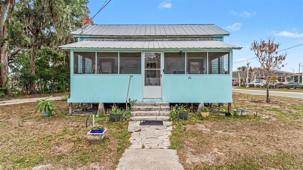 A light blue, elevated cottage with a metal roof and a screened-in front porch — 20 S LANIER AVENUE, FORT MEADE, FL