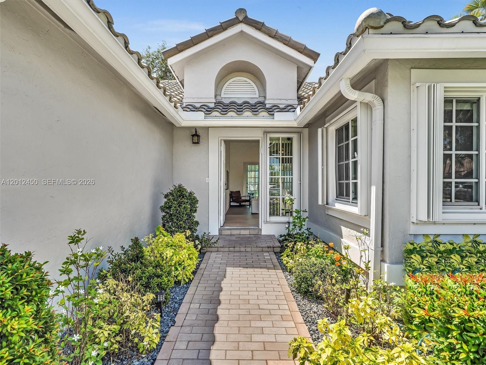 A paved walkway leads to the front entrance of a house with light-colored stucco walls — 629 Spinnaker, Weston FL 33326, WESTON, FL