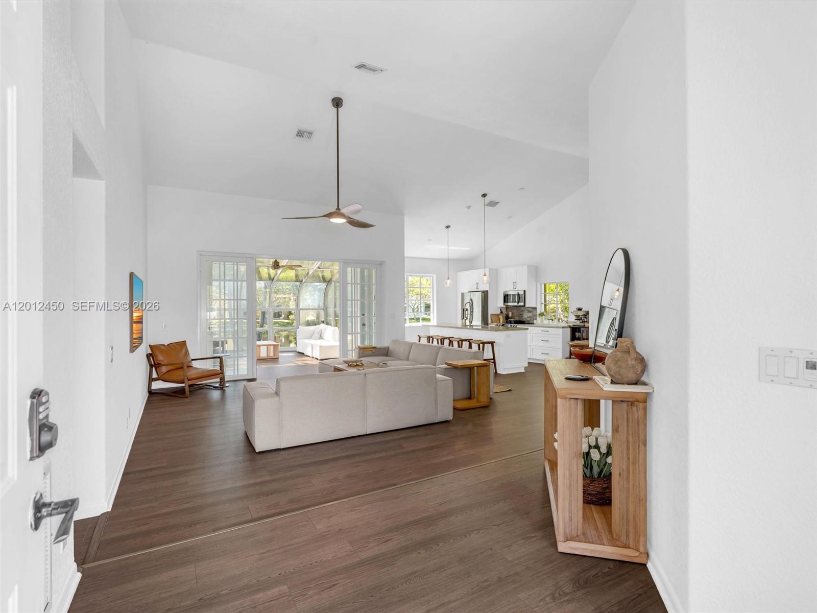 An open-concept living room and kitchen feature wood-look flooring, vaulted ceilings, and a screened patio — 629 Spinnaker, Weston FL 33326, WESTON, FL