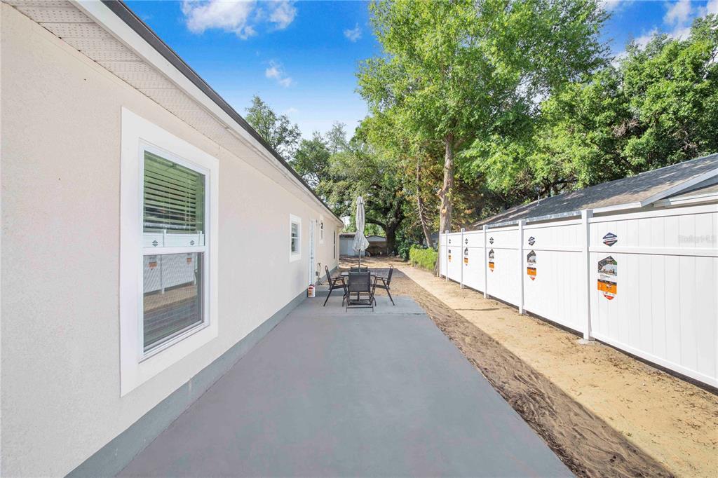 A concrete patio runs alongside a house exterior next to a white vinyl privacy fence — 3420 AVENUE T NW, WINTER HAVEN, FL