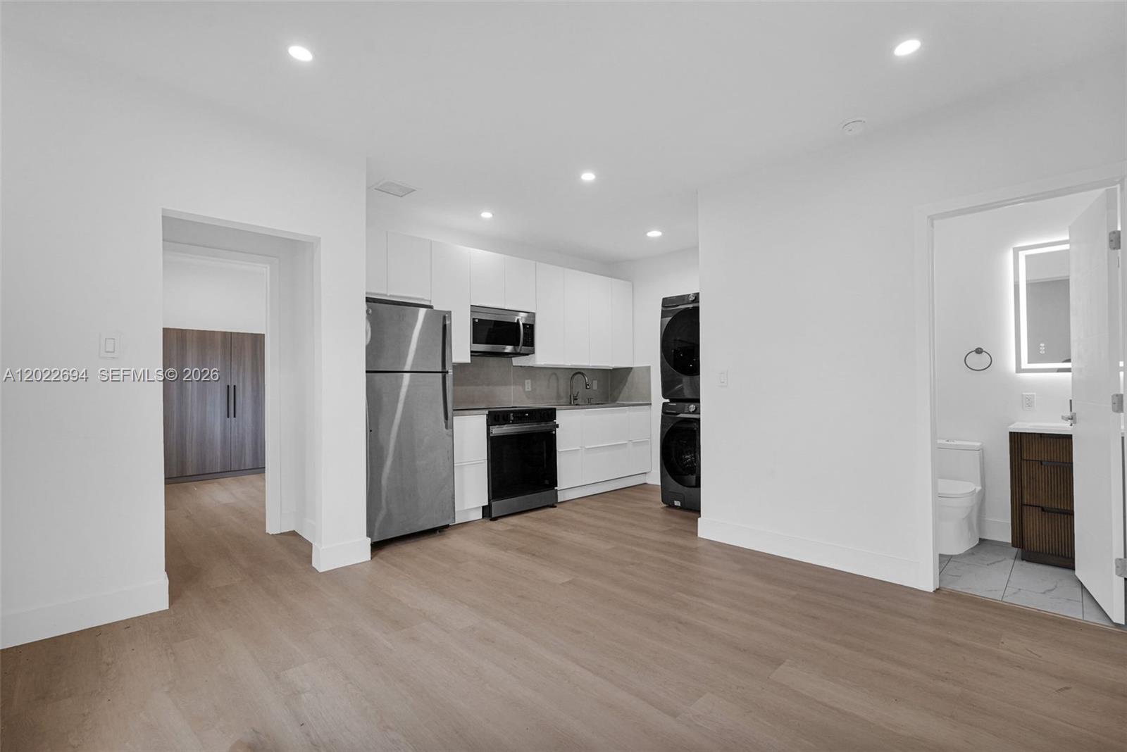 A modern kitchen with white cabinets and stainless steel appliances sits beside a laundry unit — 19 NE 48th St # 1, Miami FL 33137, MIAMI, FL