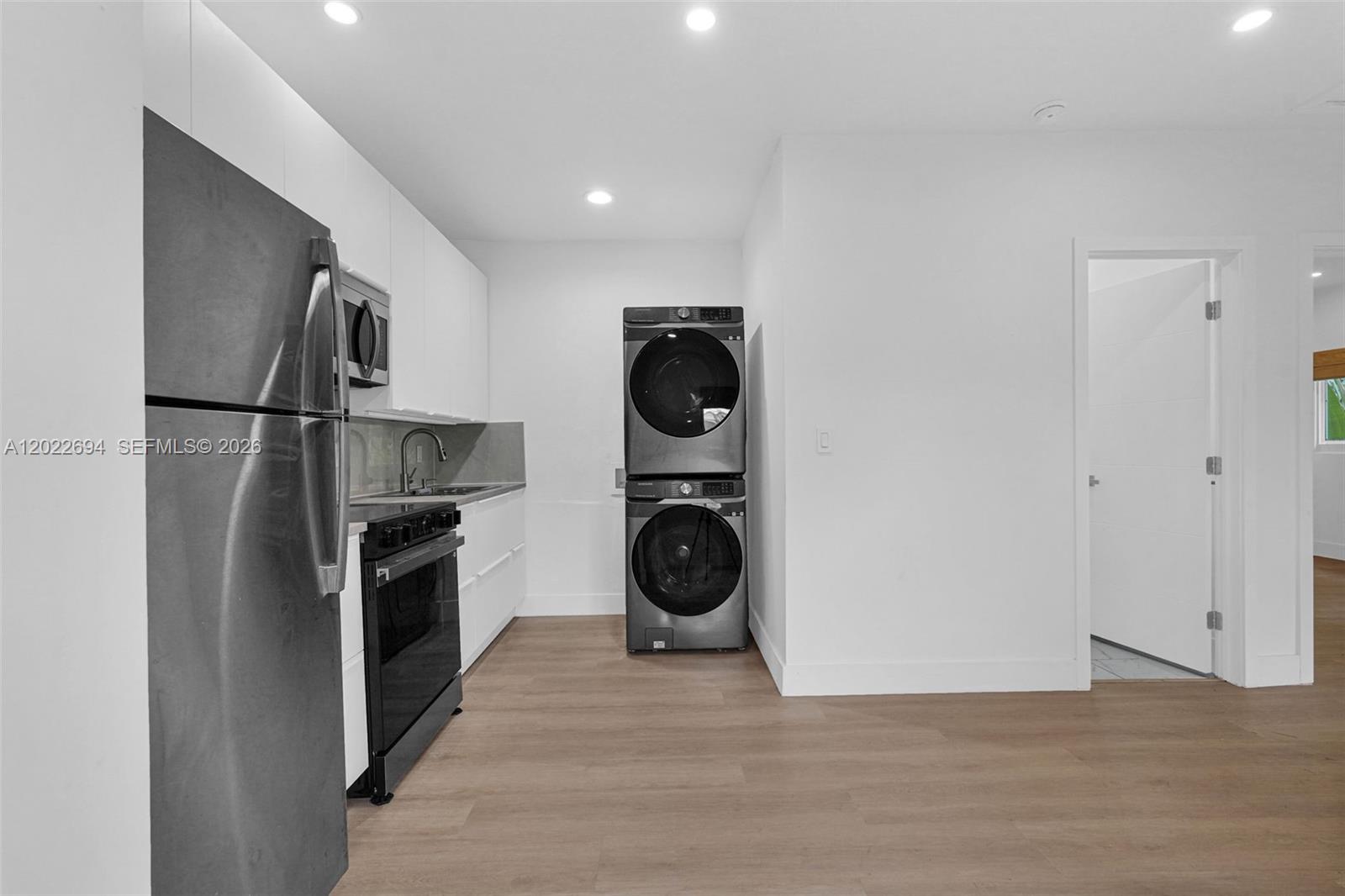 A kitchen features white cabinetry, stainless steel appliances, and a stacked washer and dryer unit — 19 NE 48th St # 1, Miami FL 33137, MIAMI, FL