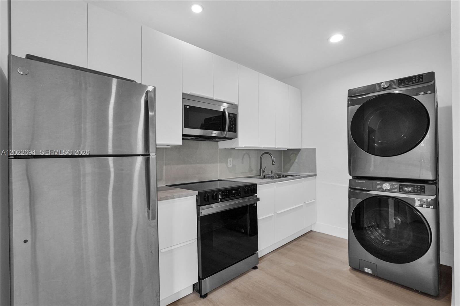 A modern kitchen features white cabinetry, stainless steel appliances, and a stacked washer and dryer — 19 NE 48th St # 1, Miami FL 33137, MIAMI, FL