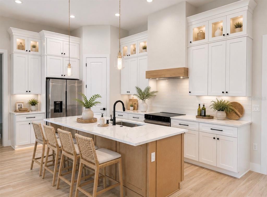 A modern kitchen features white cabinetry, a wood-toned island with seating, and stainless steel appliances — 3739 GARBETT TERRACE, NORTH PORT, FL