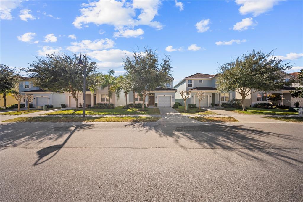 A street view of several two-story suburban houses with driveways and trees under a blue sky — 8960 BISMARCK PALM RD, KISSIMMEE, FL