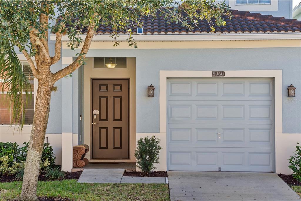 The exterior of a house features a brown front door and a light gray garage — 8960 BISMARCK PALM RD, KISSIMMEE, FL