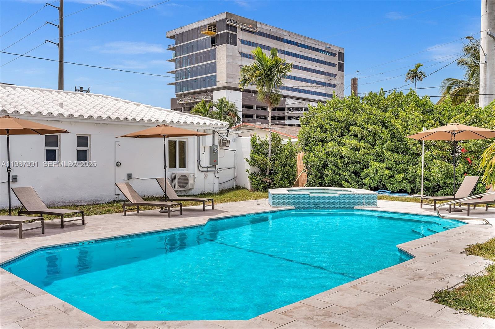 A swimming pool and hot tub are situated in a backyard with lounge chairs — 703 NE 7th St # 5, Hallandale Beach FL 33009, HALLANDALE BEACH, FL