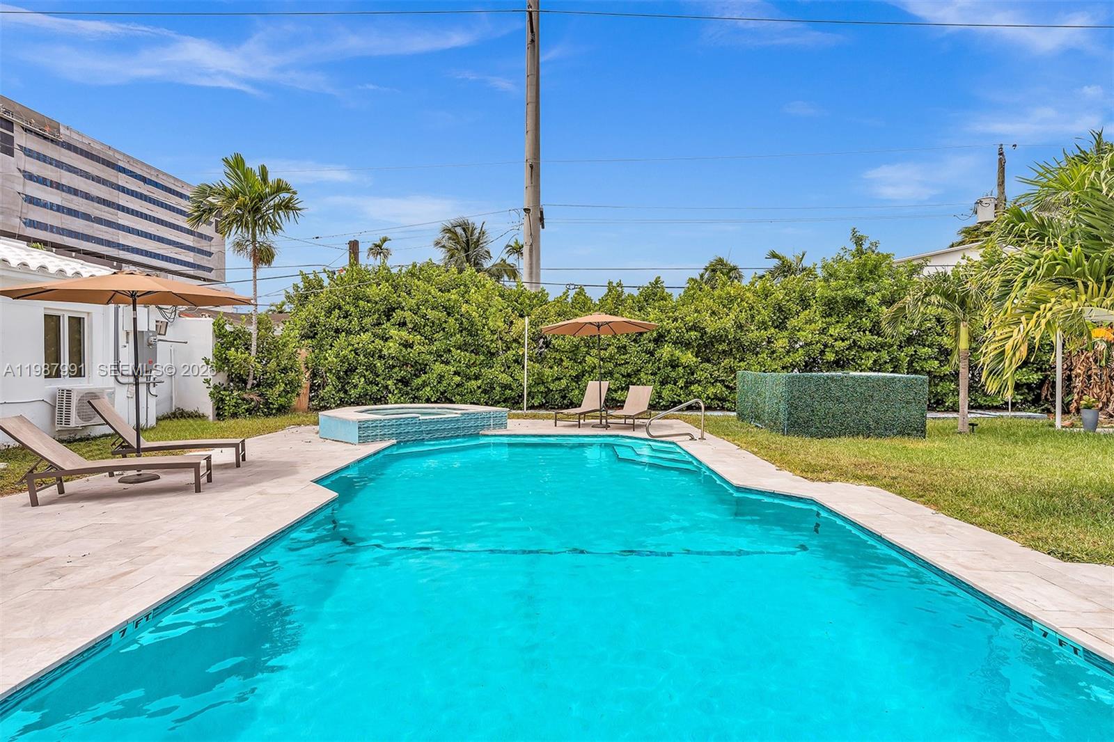 A backyard features a swimming pool with a hot tub, lounge chairs, and umbrellas — 703 NE 7th St # 5, Hallandale Beach FL 33009, HALLANDALE BEACH, FL
