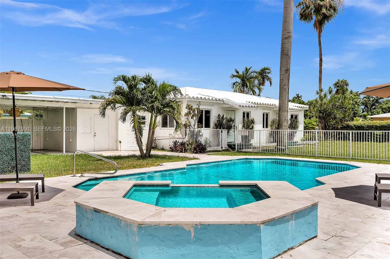 A backyard features a swimming pool, a raised spa, and a white house with palm trees — 703 NE 7th St # 5, Hallandale Beach FL 33009, HALLANDALE BEACH, FL