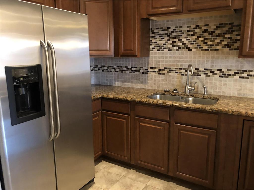 A kitchen features stainless steel appliances, dark wood cabinets, granite countertops, and a tiled backsplash — 30 LAKE VILLA WAY, KISSIMMEE, FL