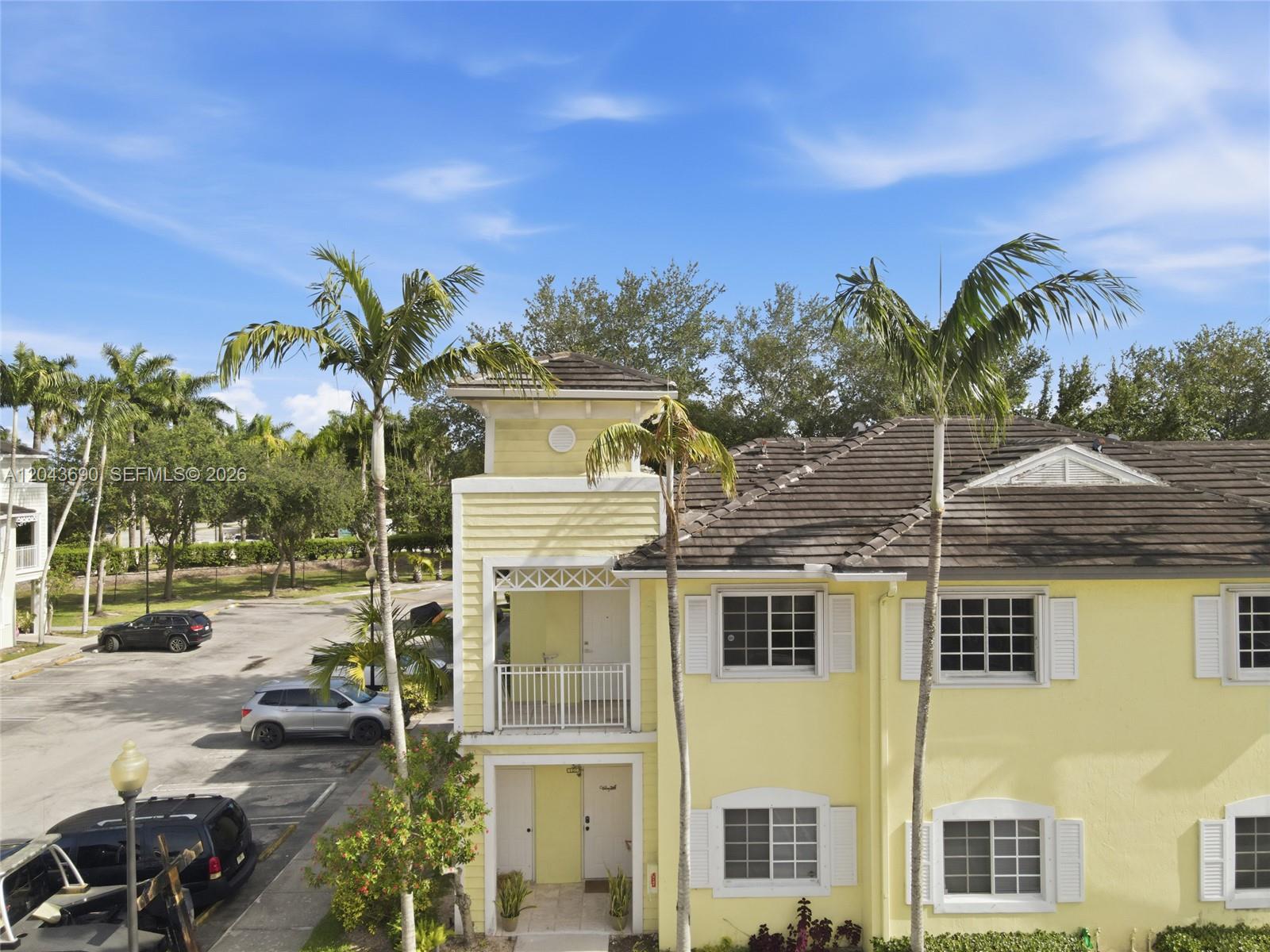 A yellow two-story building features a balcony, palm trees, and an adjacent parking lot — 2728 NE 3rd Ct # 201, Homestead FL 33033, HOMESTEAD, FL