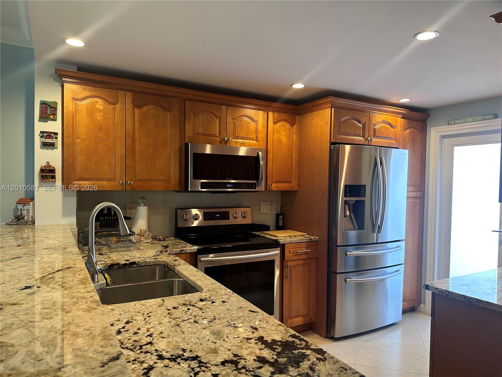A kitchen features wood cabinets, granite countertops, stainless steel appliances, and a glass-paneled door — 750 N Ocean Blvd # 310, Pompano Beach FL 33062, POMPANO BEACH, FL