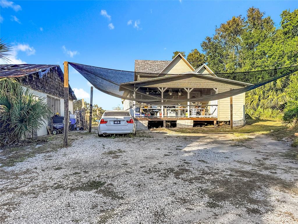 A white car is parked on a gravel driveway in front of a house with a shade sail — 7717 CLARCONA OCOEE ROAD Lot 1, ORLANDO, FL