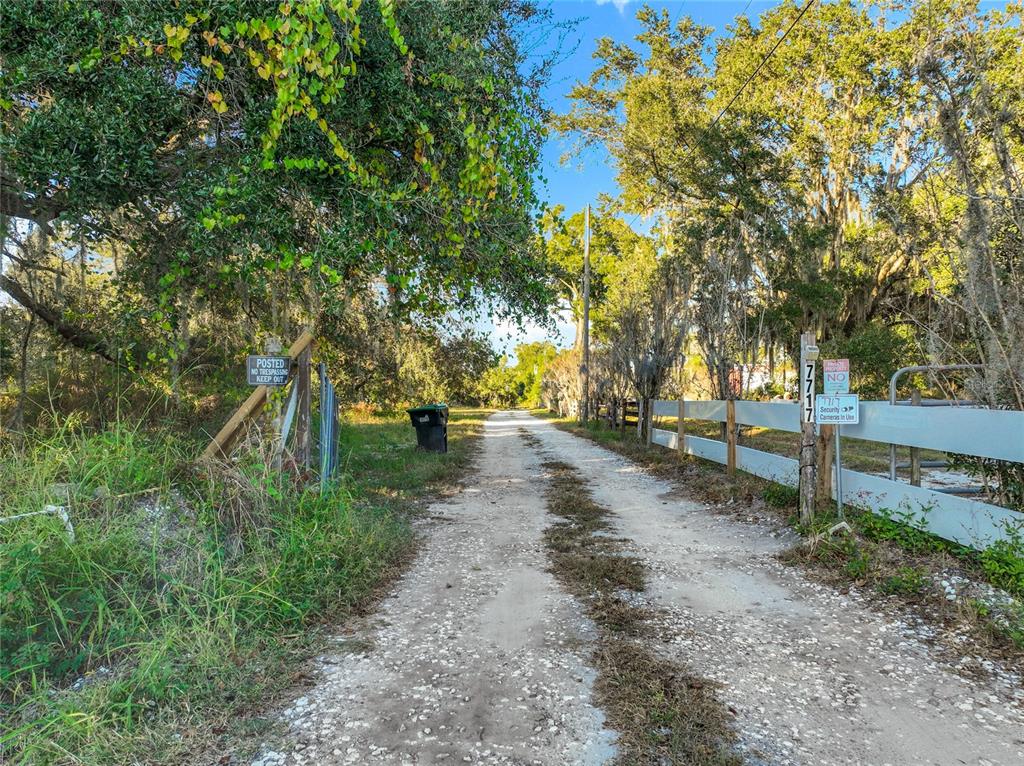 A gravel driveway leads through a wooded area toward a gated entrance with security signs — 7717 CLARCONA OCOEE ROAD Lot 1, ORLANDO, FL