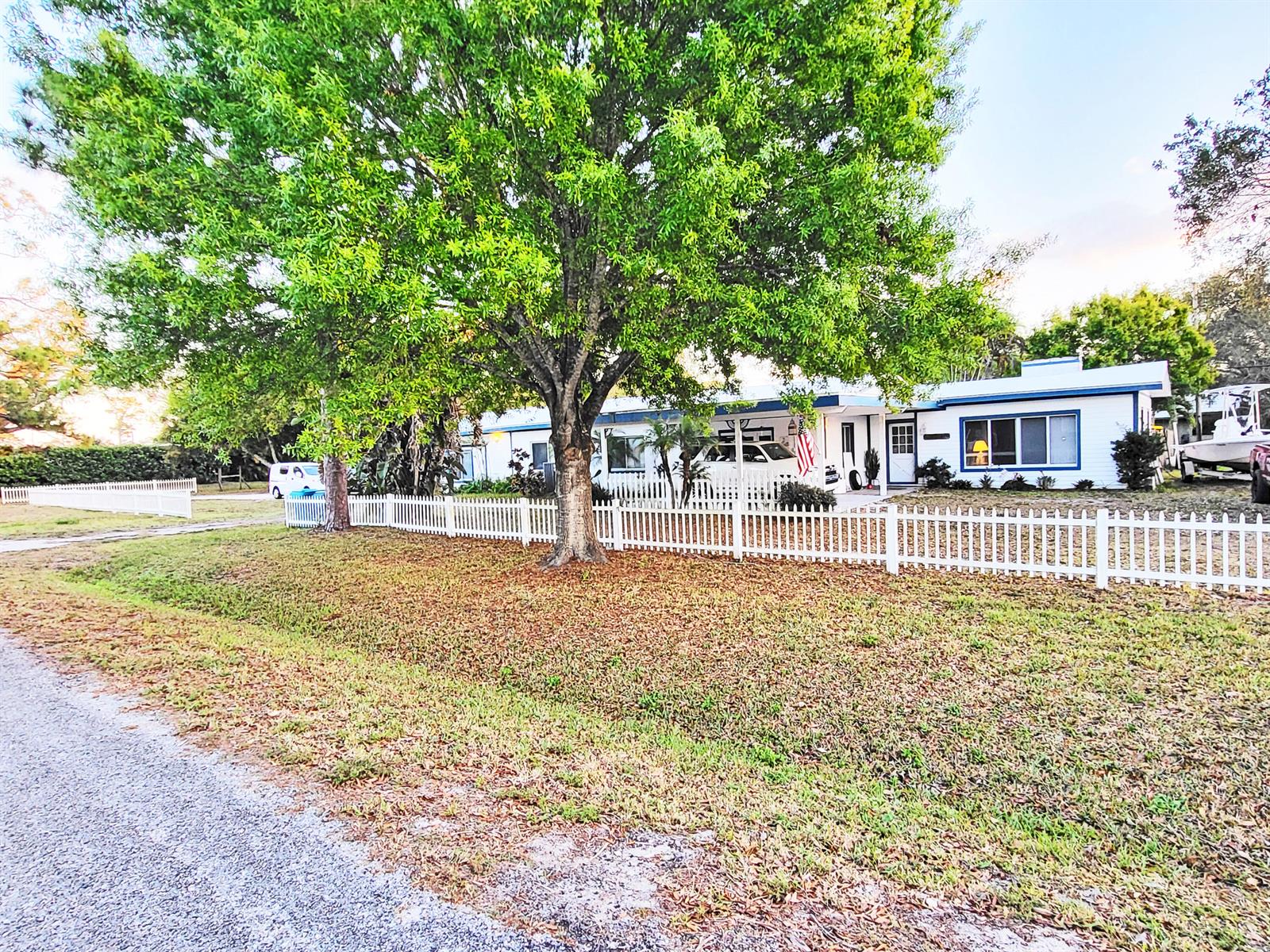 A white single-story house with a picket fence and a large tree in the yard — 203 Melton Drive, Fort Pierce FL 34982, FORT PIERCE, FL
