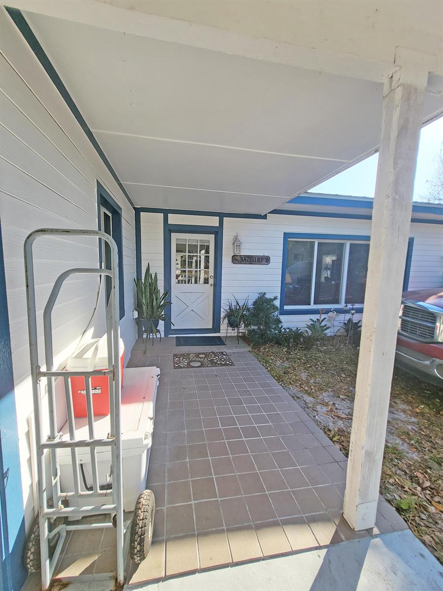 A covered porch features tiled flooring, a white front door, and a metal hand truck — 203 Melton Drive, Fort Pierce FL 34982, FORT PIERCE, FL