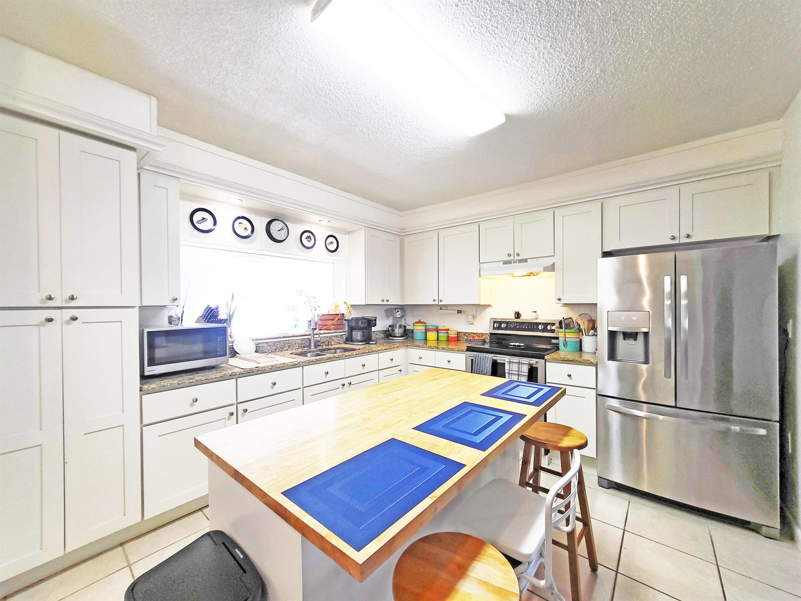 A kitchen features white cabinets, stainless steel appliances, and a wooden island with stools — 203 Melton Drive, Fort Pierce FL 34982, FORT PIERCE, FL