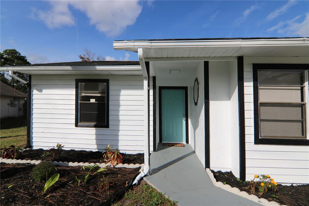 A white house exterior features a light blue front door and a gray concrete walkway — 711 KEMPTEN STREET NW, PALM BAY, FL
