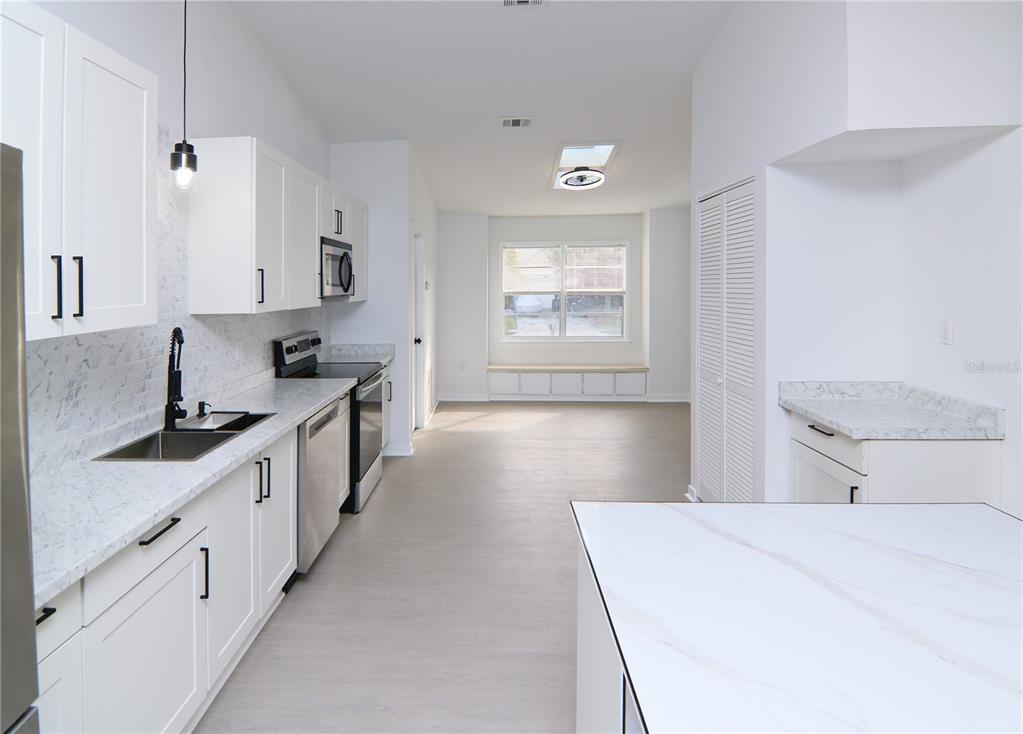 A modern kitchen features white cabinets, marble-look countertops, stainless steel appliances, and a window seat — 711 KEMPTEN STREET NW, PALM BAY, FL