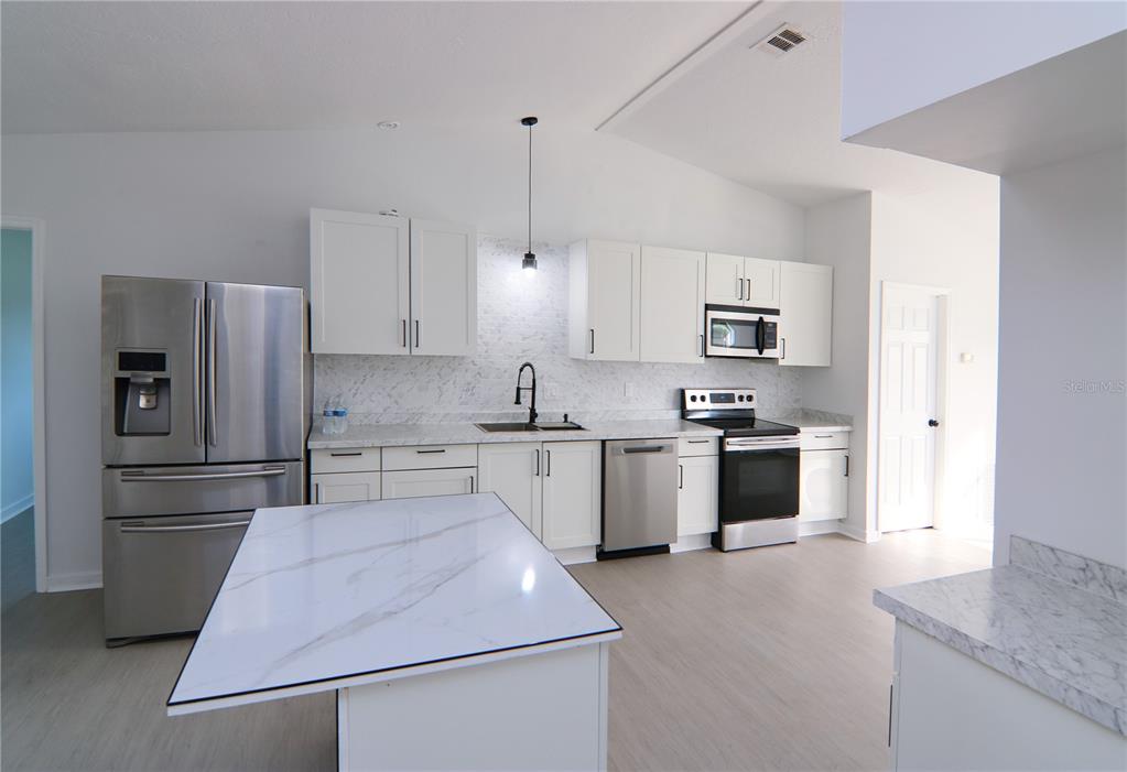 A modern kitchen features white cabinets, marble-look countertops, stainless steel appliances, and a central island — 711 KEMPTEN STREET NW, PALM BAY, FL