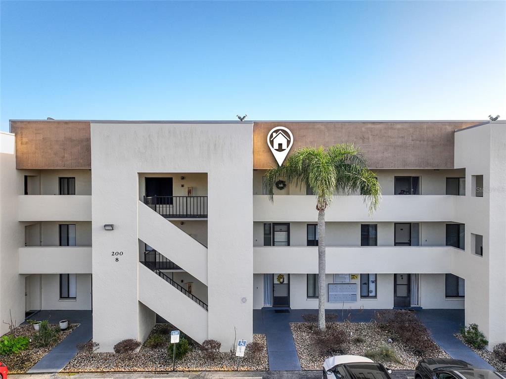 A three-story apartment building exterior features a central staircase, balconies, and a palm tree — 200 INTERNATIONAL DRIVE UNIT 815, CAPE CANAVERAL, FL