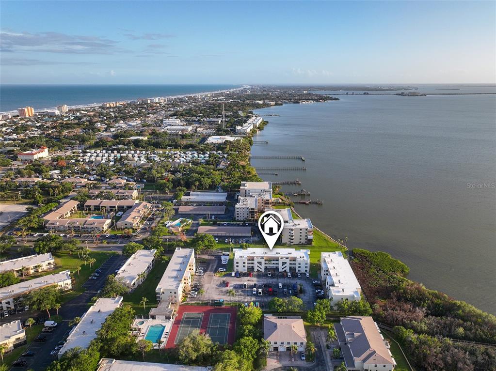 An aerial view shows a waterfront apartment complex with a pool and tennis courts — 200 INTERNATIONAL DRIVE UNIT 815, CAPE CANAVERAL, FL