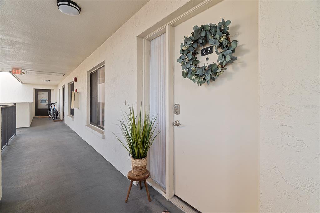 An exterior hallway shows a white door with a wreath, a potted plant, and a bicycle — 200 INTERNATIONAL DRIVE UNIT 815, CAPE CANAVERAL, FL