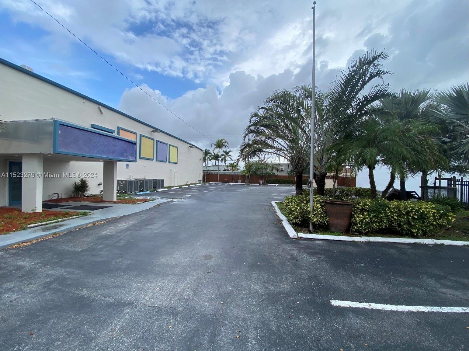 A paved parking lot sits beside a building with a blue awning and palm trees — 2055 Liberty St, Hollywood FL 33020, HOLLYWOOD, FL