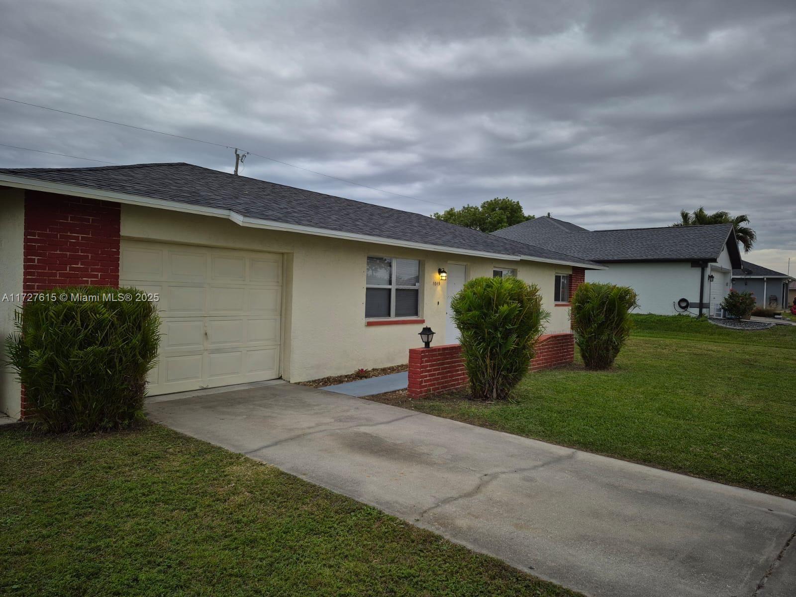 A single-story house with a beige stucco exterior, red brick accents, and a concrete driveway — 1019 NW 7TH PLACE, Cape Coral FL 33993, CAPE CORAL, FL