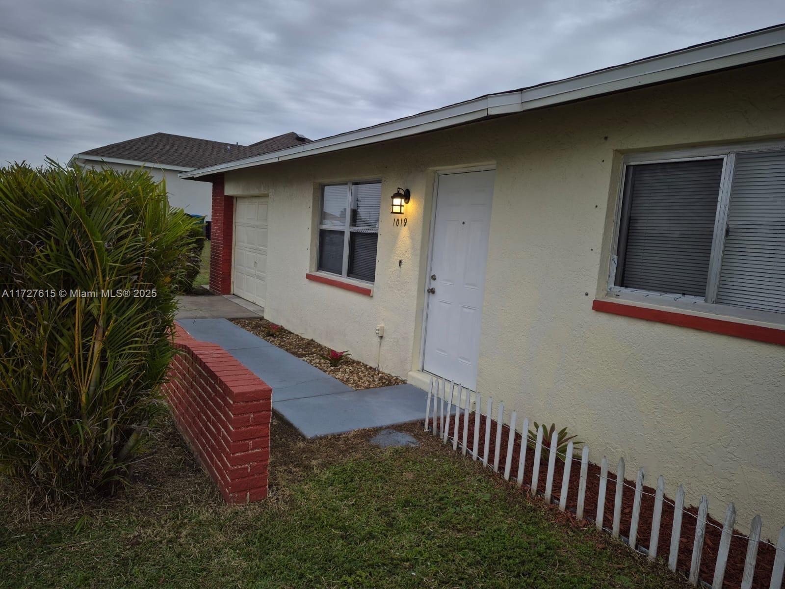 The exterior of a single-story house features a white door, brick accents, and a small fence — 1019 NW 7TH PLACE, Cape Coral FL 33993, CAPE CORAL, FL