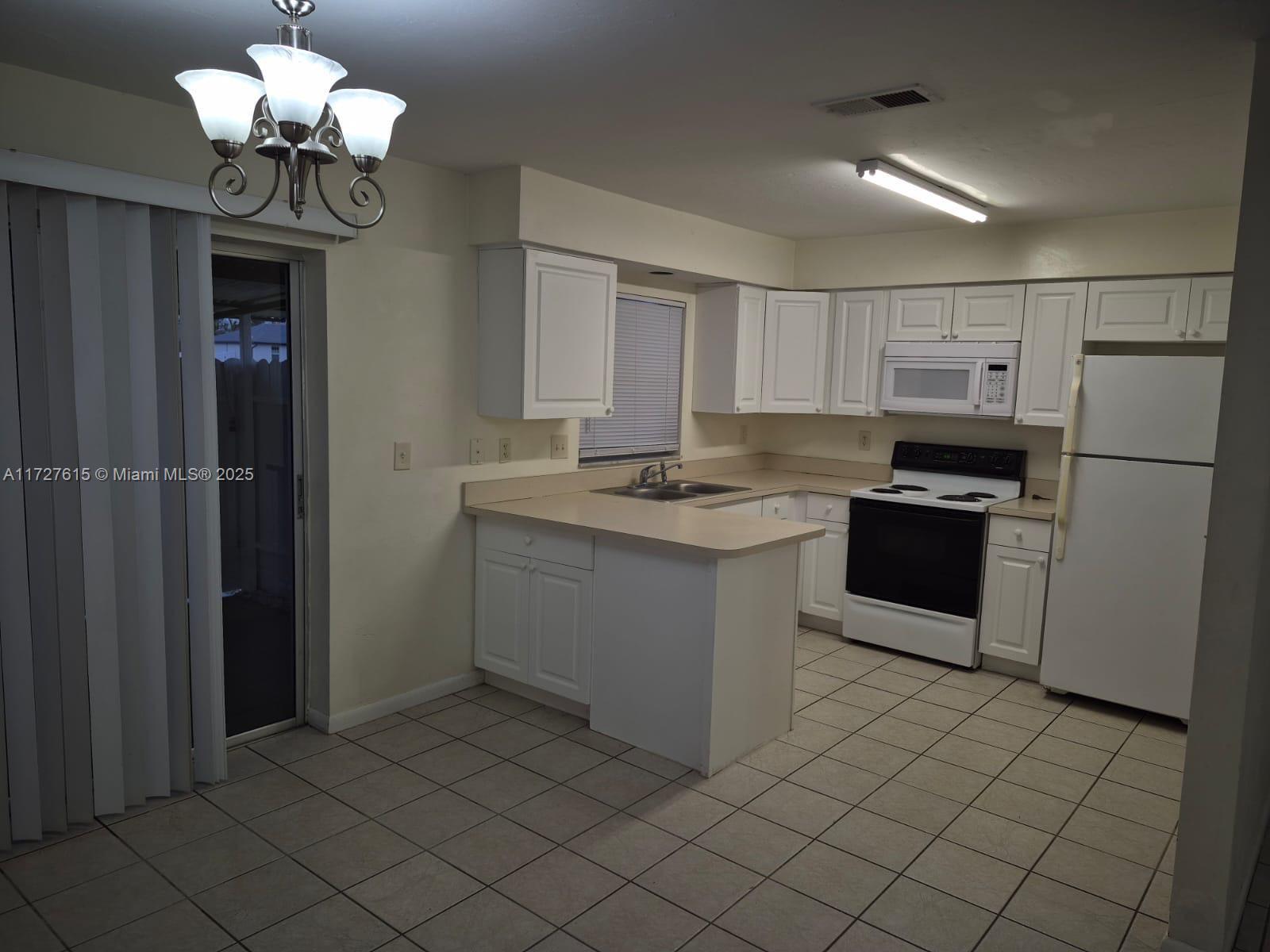 A kitchen features white cabinets, light countertops, tile flooring, and a sliding glass door — 1019 NW 7TH PLACE, Cape Coral FL 33993, CAPE CORAL, FL