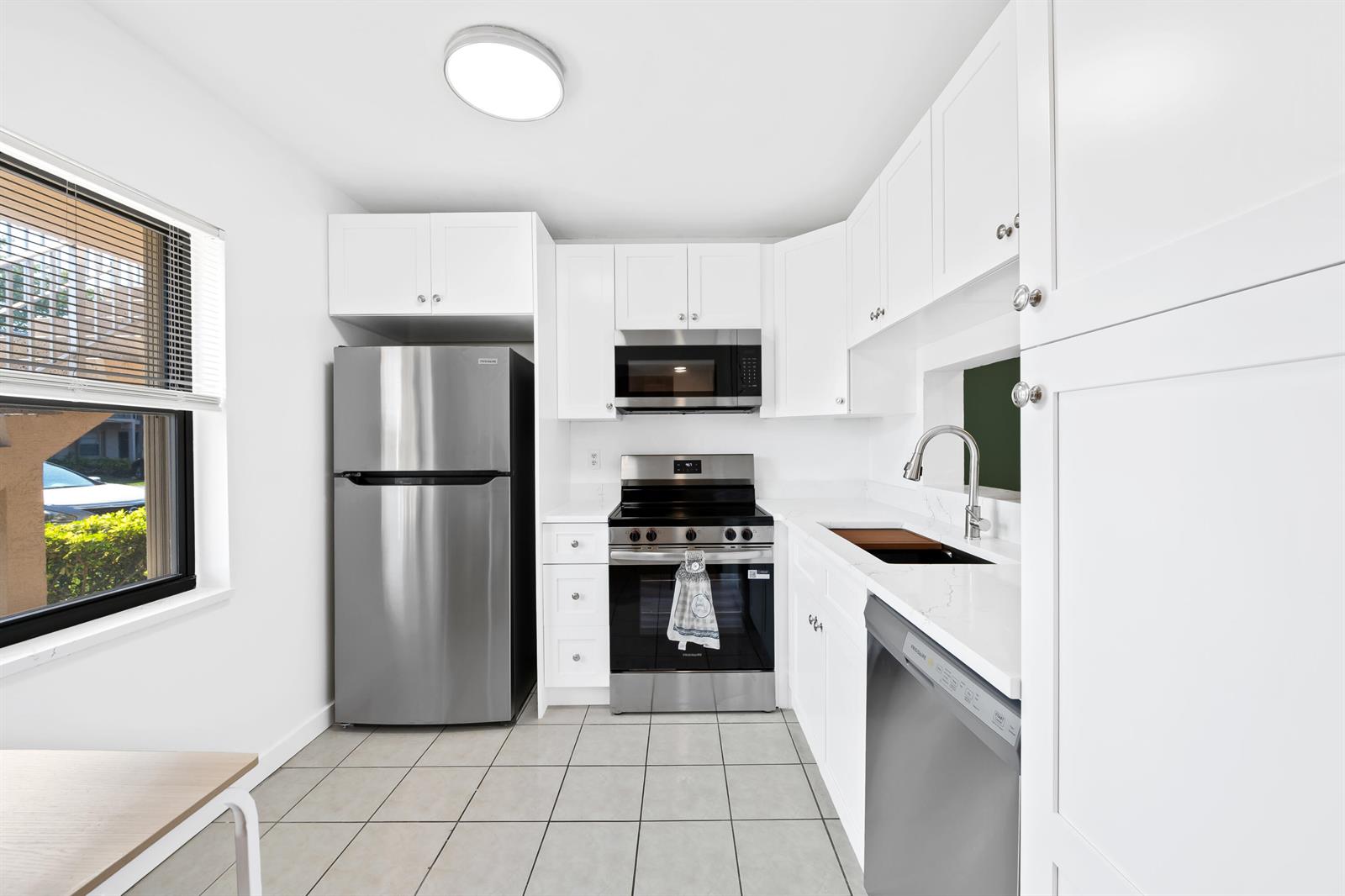A bright kitchen features white cabinets, stainless steel appliances, quartz countertops, and light tile flooring — 5570 Lakeside Drive # 102, Margate FL 33063, MARGATE, FL